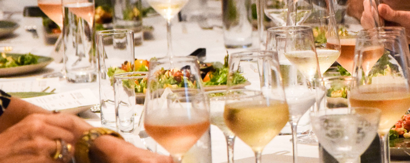 people sitting at event table with place settings, wine glasses, and salads